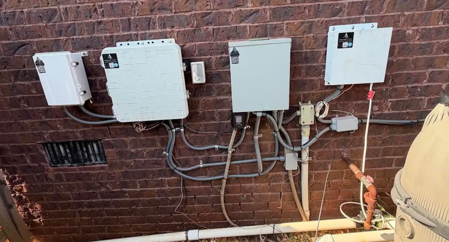 Labeled and asset-tagged pool automation and control enclosures mounted on a brick wall