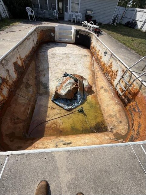 Drained pool shell with heavy corrosion, failed surface and standing groundwater before renovation
